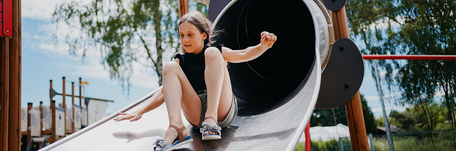 A girl exists a tube slide, with a smile on her face at a playground.